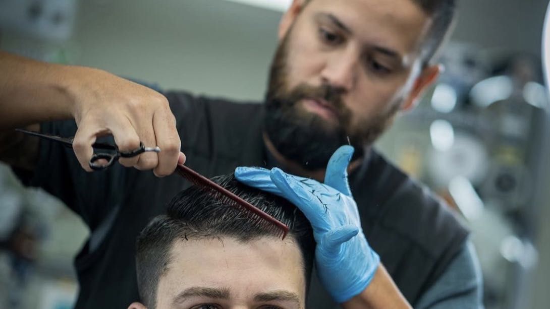 Pedro cutting a client's hair with a comb and scissors